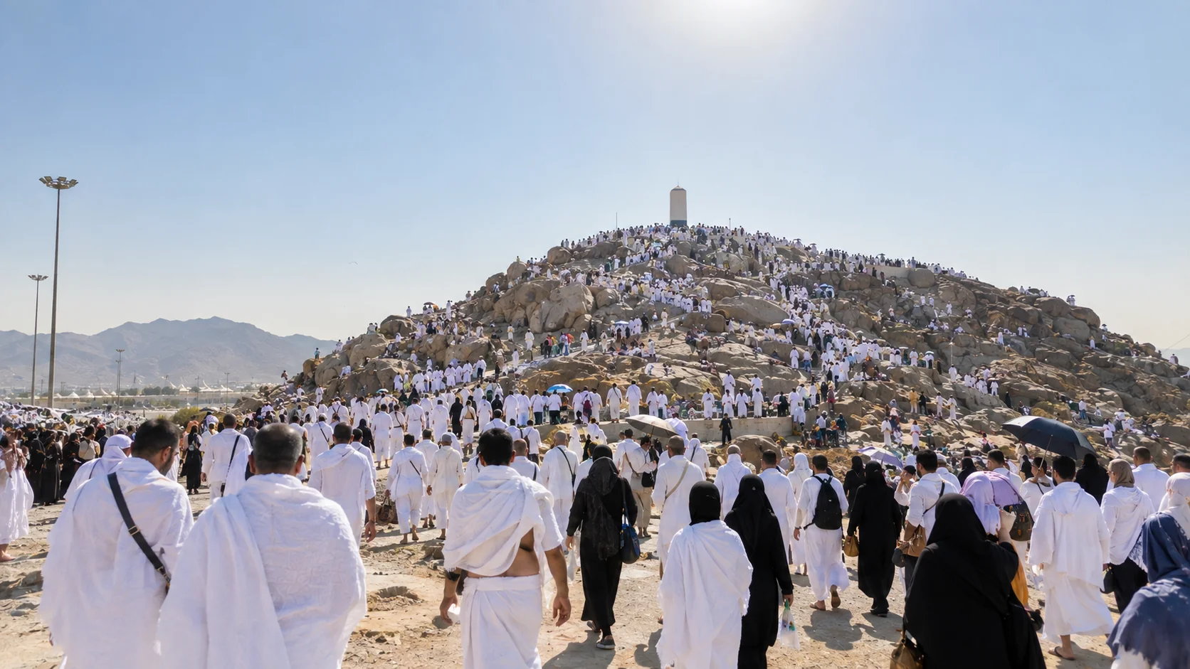 Arafat'ta vakfe: tepeye doğru yürüyen ihramlı kalabalık, gün ortası sıcak ışık, geniş manzara